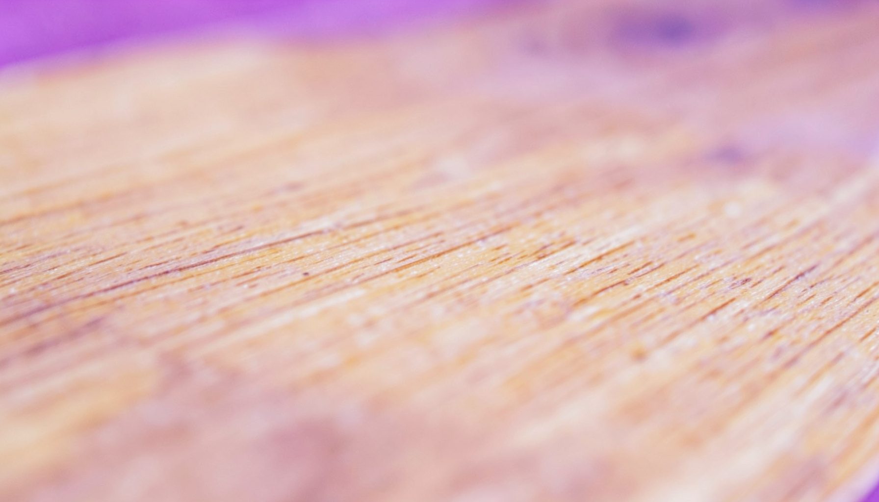 A warm-toned close-up of smooth light wood grain with subtle beige and honey hues, showing the natural texture of a folding table surface.