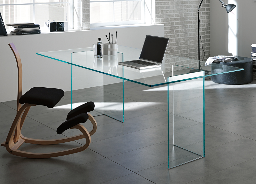 Home office with glass desk, wooden ergonomic kneeling chair, laptop, desk lamp, and brick accent wall